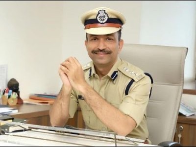 Portrait of Chirag Koradia in police uniform and peaked cap, seated at his office desk with his hands folded.