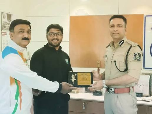 Chirag Koradia in police uniform at an official engagement, taking part in the presentation of a commemorative memento with two other people.